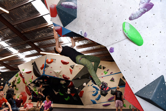 man performing a dynamic bouldering move in a bouldering gym on an overhung wall