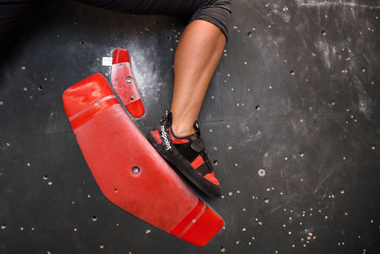 Boulderer wearing Redpoint Climbing Australia climbing shoes standing on red hold